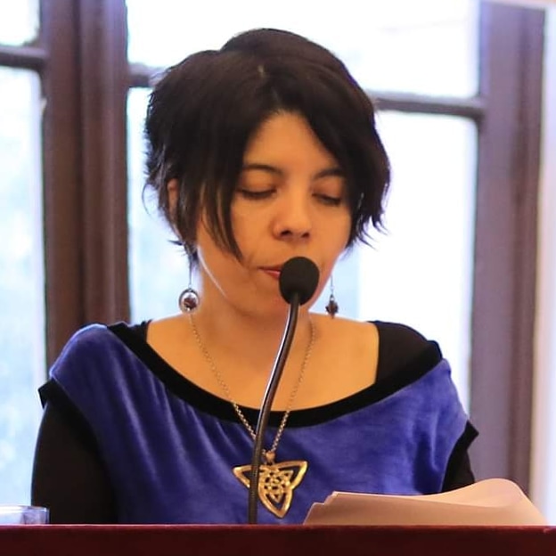 Fotografia de Mirka Arriagada en una conferencia, leyendo a viva voz un texto